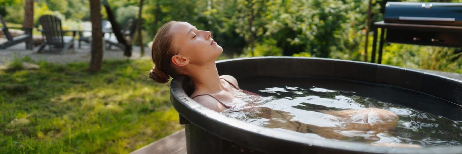 Woman practising cold water immersion in a backyard cold plunge tub surrounded by nature.