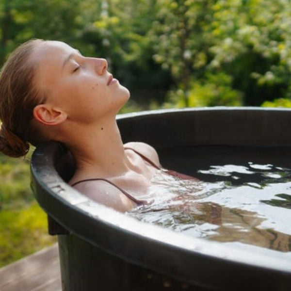 Woman practising cold water immersion in a backyard cold plunge tub surrounded by nature.