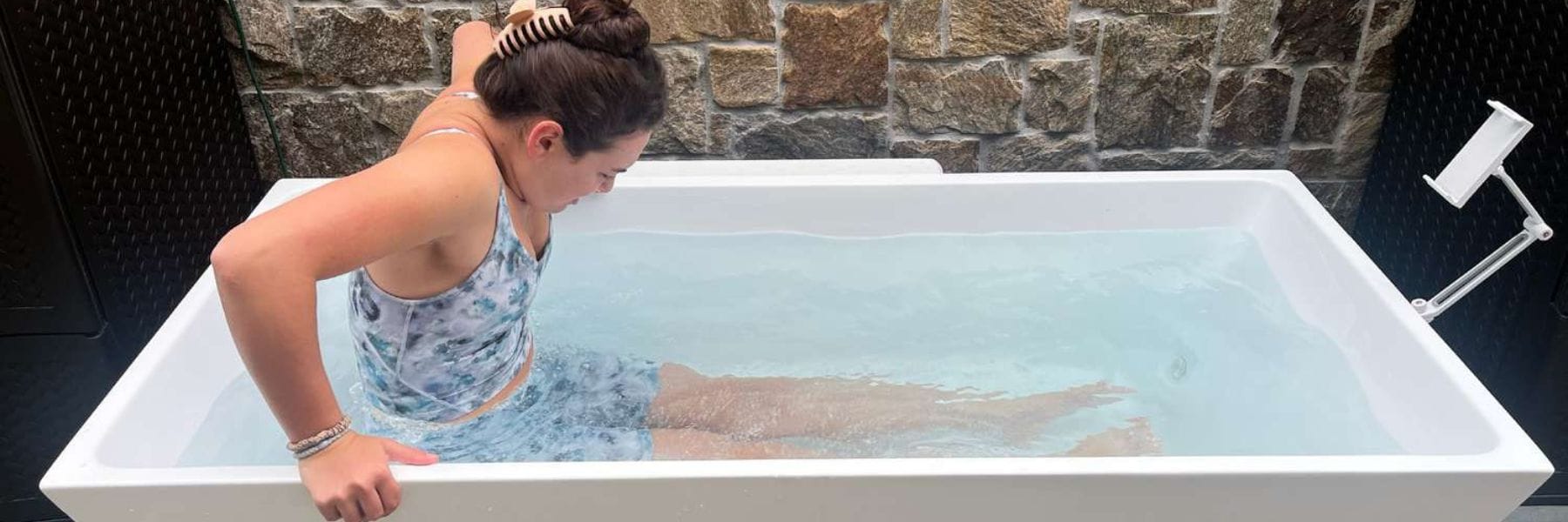 Woman slowly entering a cold plunge tub for cold water therapy in an outdoor ice bath