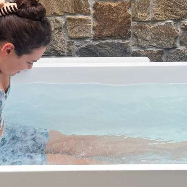 Woman slowly entering a cold plunge tub for cold water therapy in an outdoor ice bath