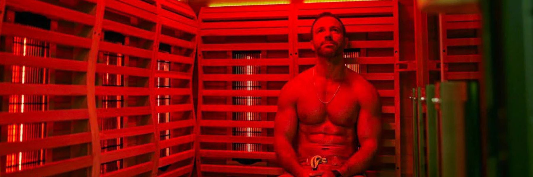 Man sitting in infrared sauna with red light therapy panels, following a consistent wellness routine
