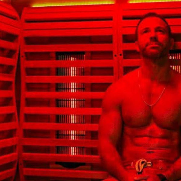 Man sitting in infrared sauna with red light therapy panels, following a consistent wellness routine