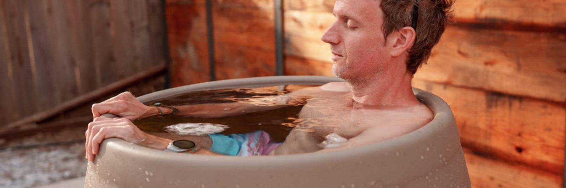 Athlete sitting in an outdoor ice bath tub filled with cold water and ice for post-workout recovery.