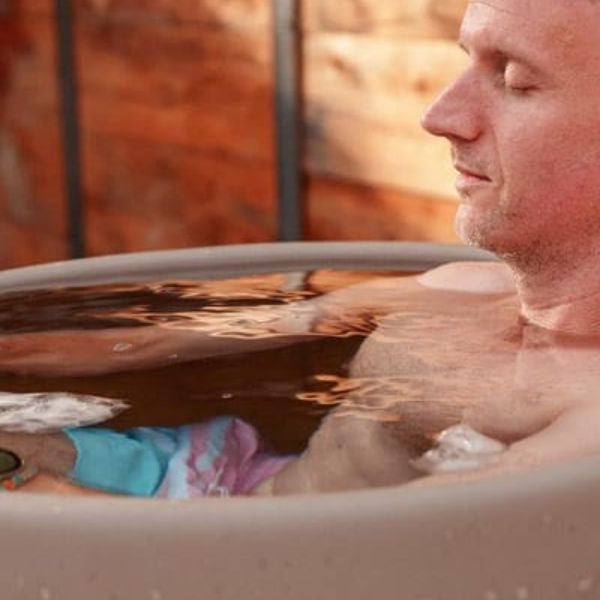 Athlete sitting in an outdoor ice bath tub filled with cold water and ice for post-workout recovery.