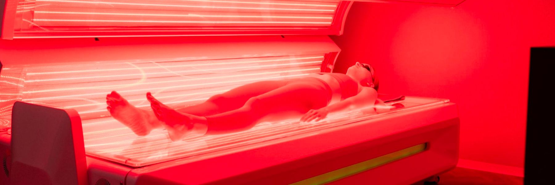 Person using full-body red light therapy bed, exploring safety concerns and potential links to skin cancer