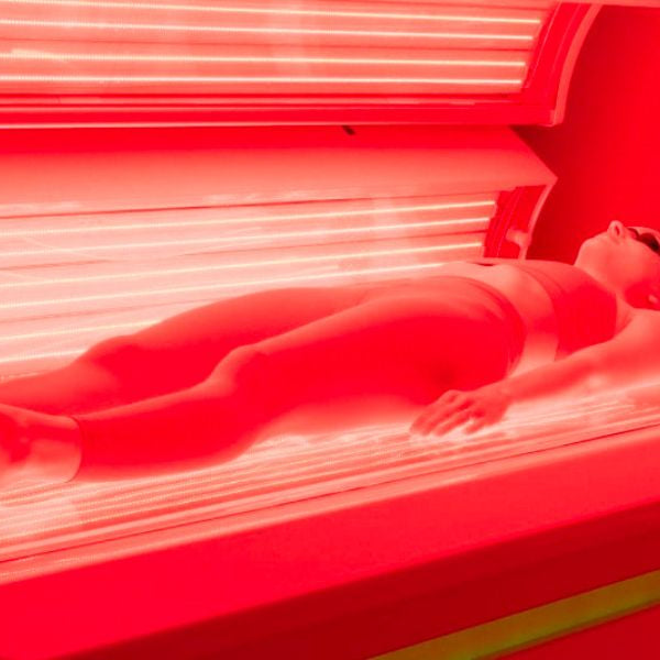 Person using full-body red light therapy bed, exploring safety concerns and potential links to skin cancer