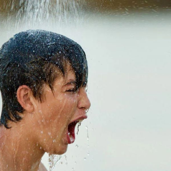Practising controlled breathing while standing under a cold shower during a cold plunge routine.