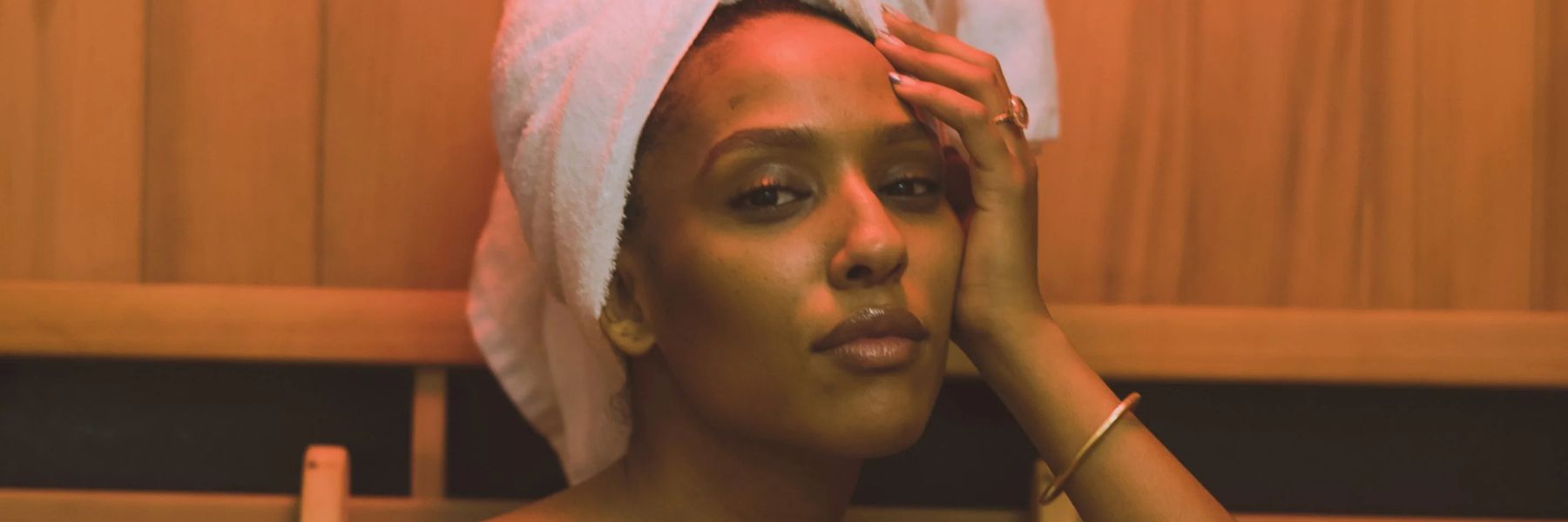 Woman with towel in sauna with warm light, illustrating skin detox, hydration, and glow-enhancing benefits