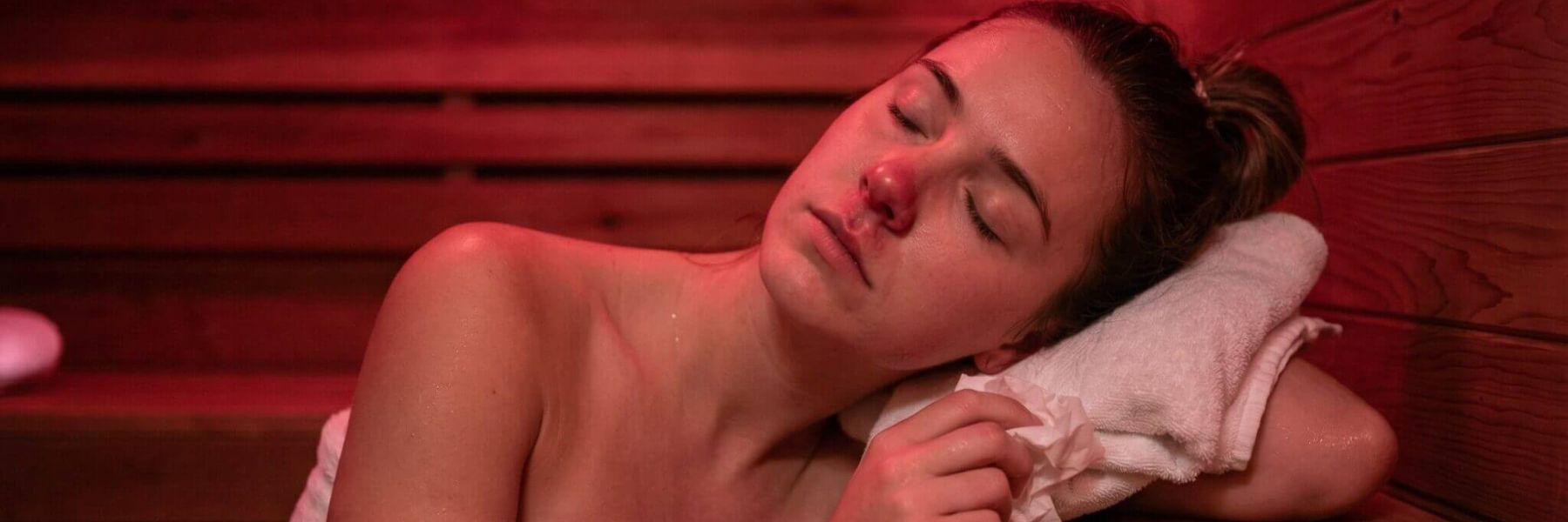 Woman relaxing in infrared sauna with red light therapy, promoting facial skin recovery and hydration