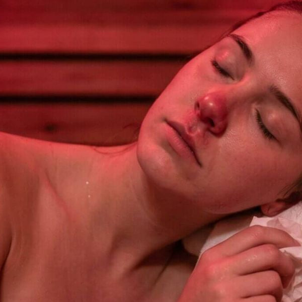 Woman relaxing in infrared sauna with red light therapy, promoting facial skin recovery and hydration