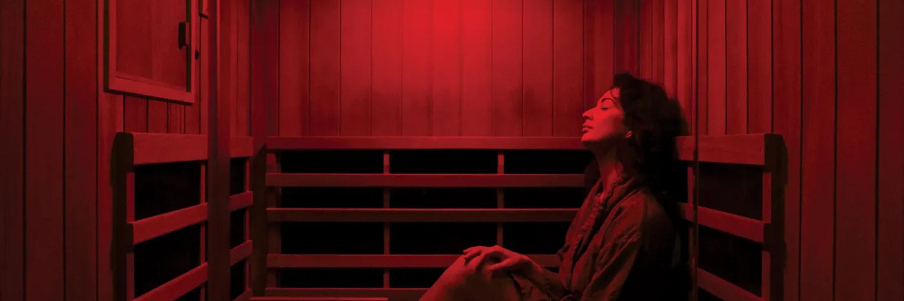 Woman relaxing in infrared sauna with red light therapy, supporting overall wellness and recovery