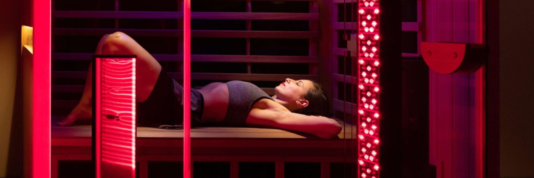 Woman relaxing under red light therapy panels in infrared sauna, promoting recovery and muscle relaxation