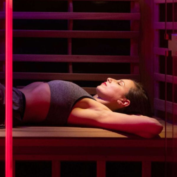 Woman relaxing under red light therapy panels in infrared sauna, promoting recovery and muscle relaxation