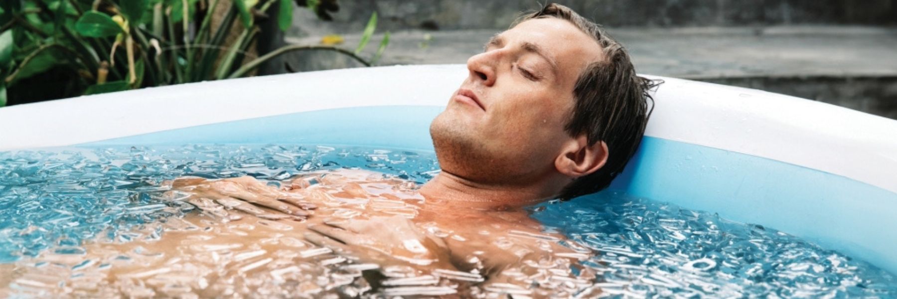 Person stepping into a cold plunge tub for ice bath recovery therapy outdoors.