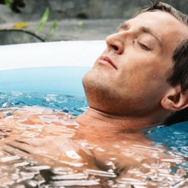 Person stepping into a cold plunge tub for ice bath recovery therapy outdoors.