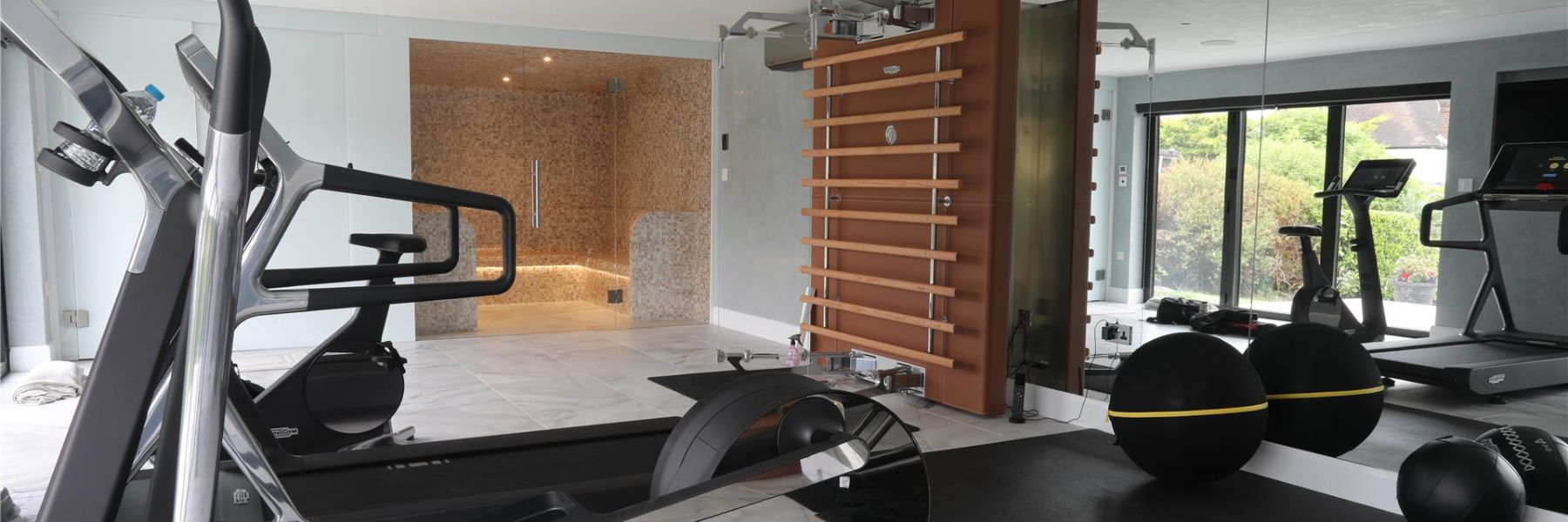 Modern home gym with steam room in the background, showing integrated wellness and fitness space