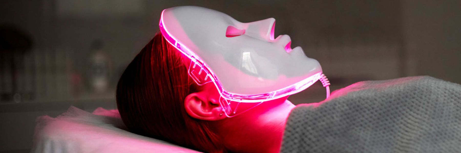 Woman wearing LED red light therapy face mask at home for skin rejuvenation and anti-aging treatment