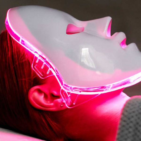 Woman wearing LED red light therapy face mask at home for skin rejuvenation and anti-aging treatment