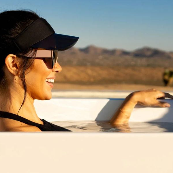 Woman relaxing in a cold plunge tub in the sun, showing contrast between perceived benefits and possible risks