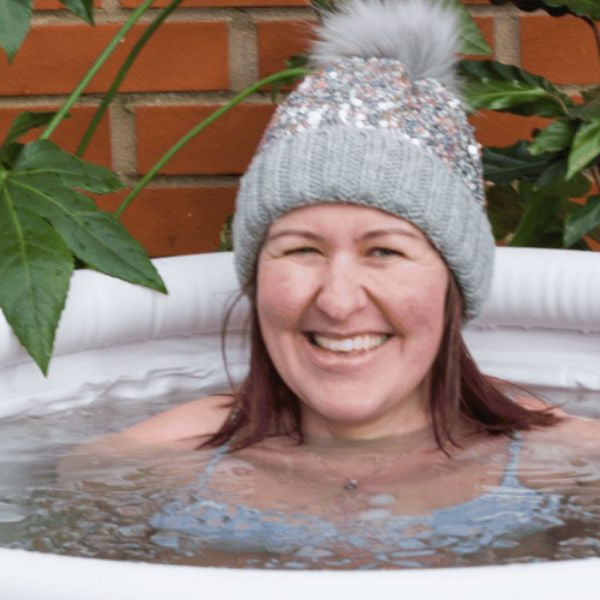 Person wearing a wool hat while relaxing in an outdoor ice bath tub during cold plunge recovery session