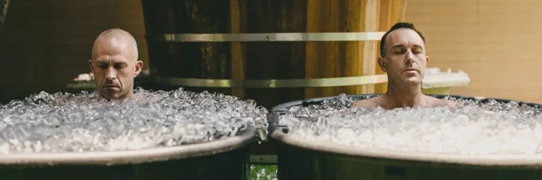 Men sitting in metal ice bath tubs filled with ice during a cold plunge recovery session.