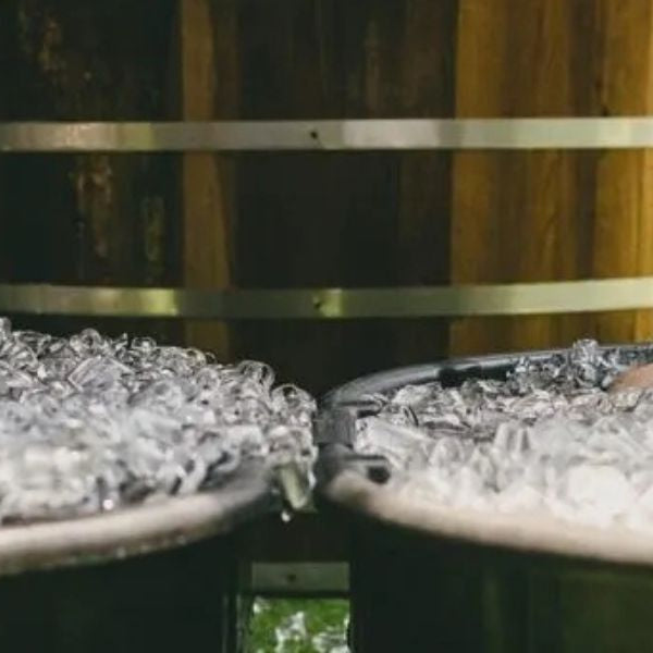 Men sitting in metal ice bath tubs filled with ice during a cold plunge recovery session.