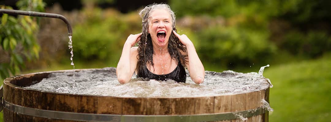 Woman enjoying an energising cold plunge in a wooden ice bath tub during outdoor cold therapy