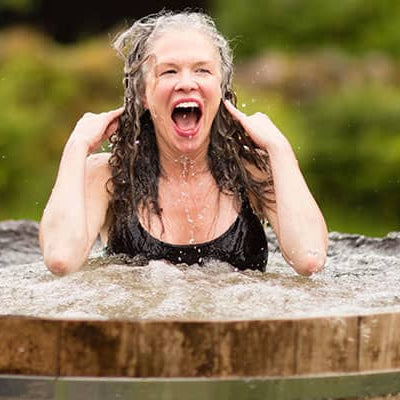 Woman enjoying an energising cold plunge in a wooden ice bath tub during outdoor cold therapy