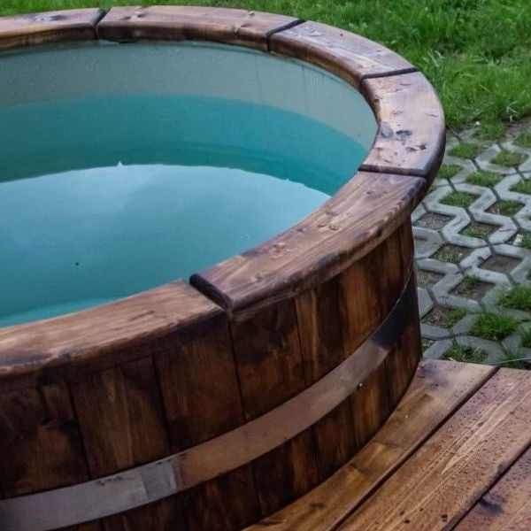Outdoor wooden cold plunge tub filled with cold water next to a hot tub in a garden wellness setup.