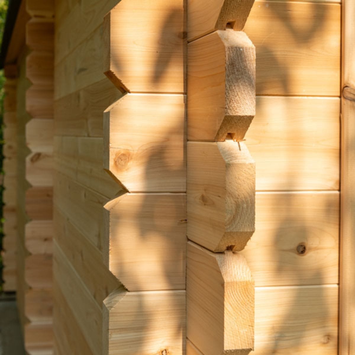 Close-up of a wooden log cabin wall with sunlight casting shadows.