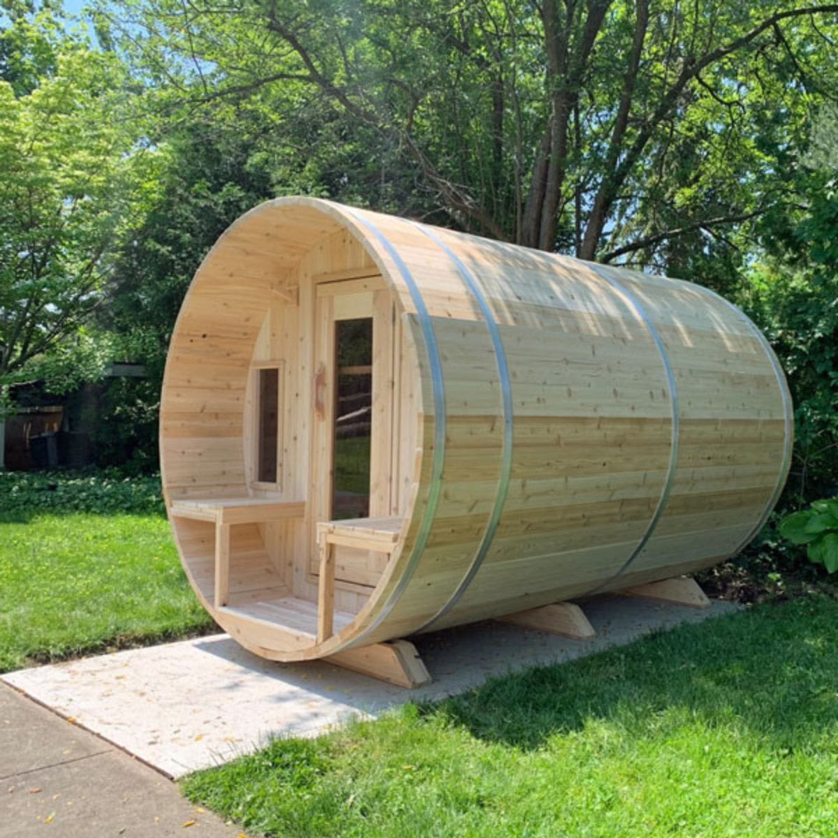 Wooden barrel-shaped sauna in a garden setting with greenery.