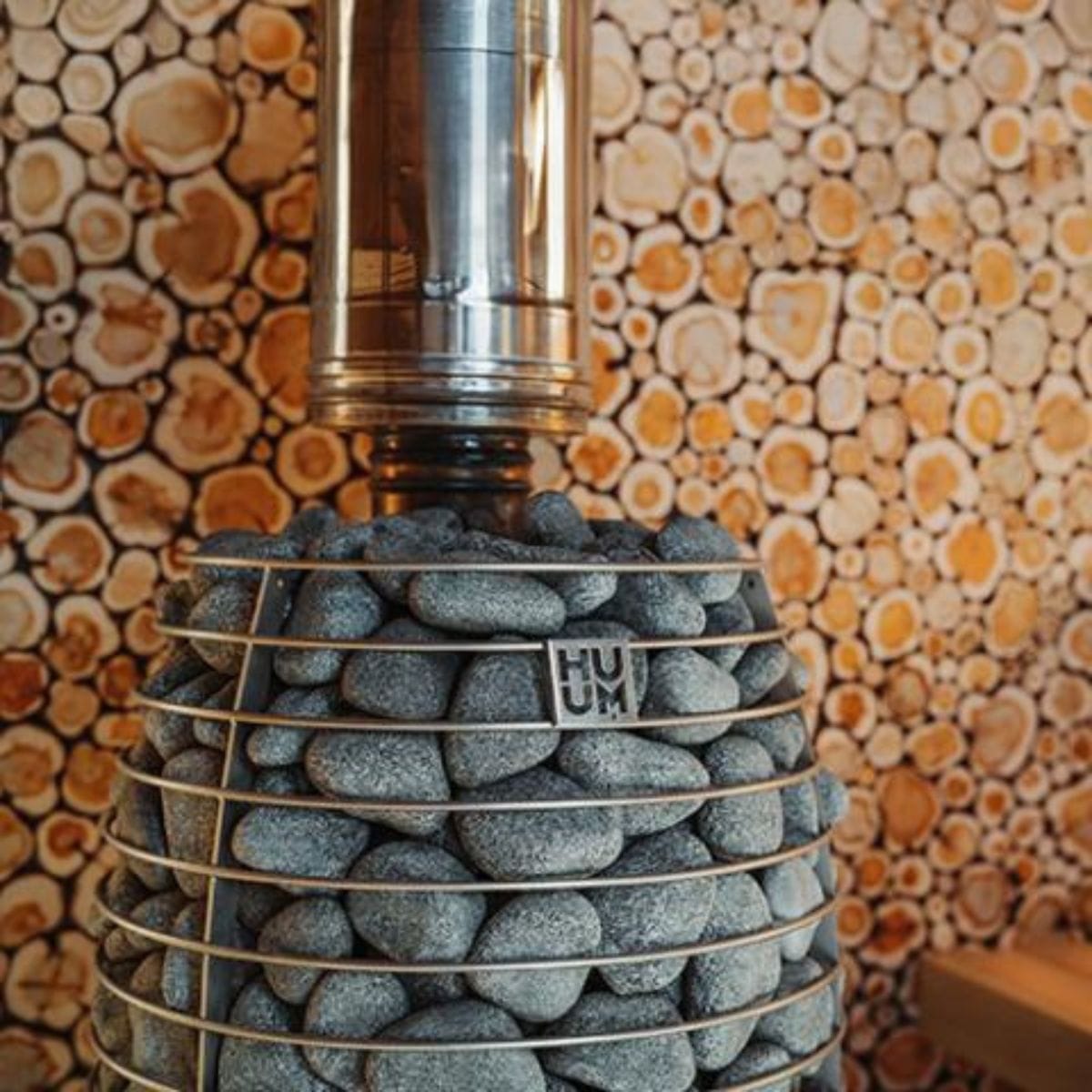 Decorative sauna heater stove made of stones with a metallic top against a patterned wall.