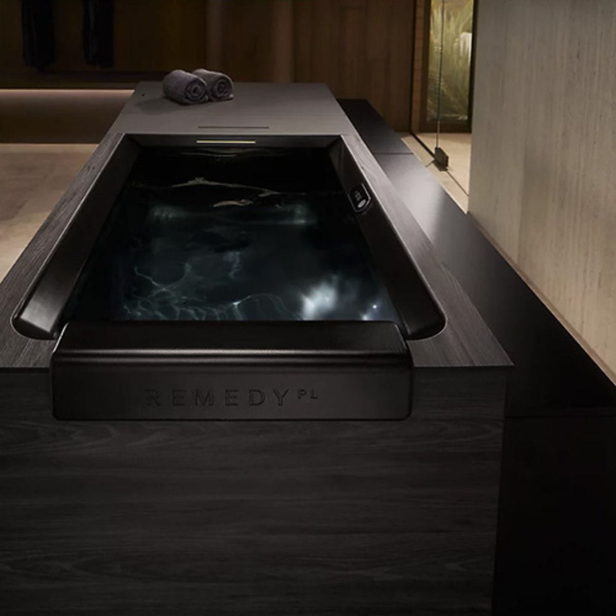 Modern plunge tub with water in a dimly lit room, featuring the brand 'Remedy'.