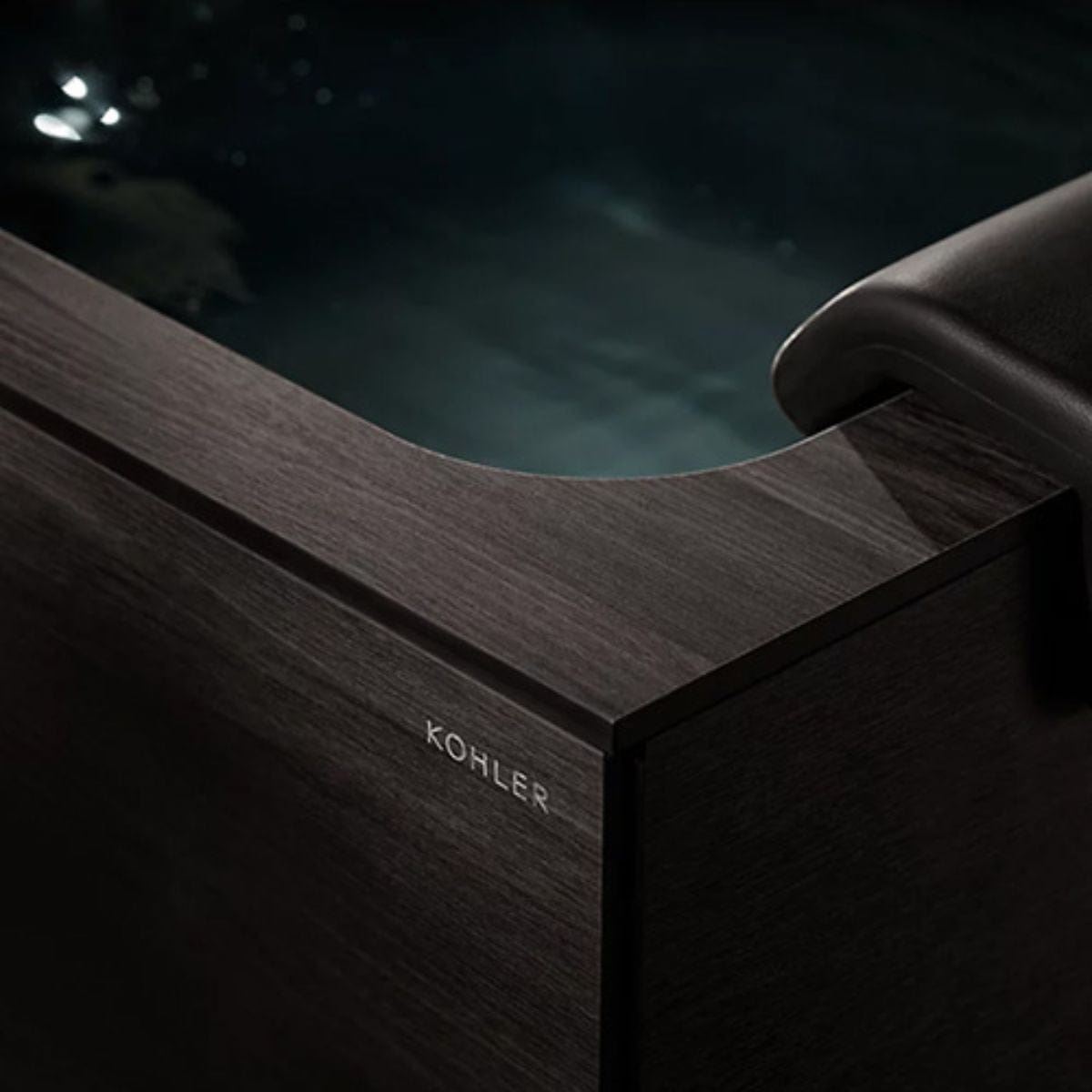 Wooden bathtub with KOHLER branding by a pool at night