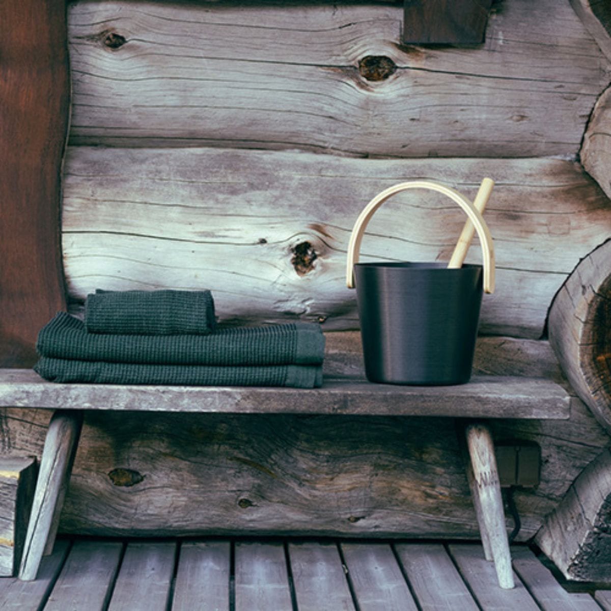 Black bucket with wooden handle on a wooden shelf against a rustic wooden wall.