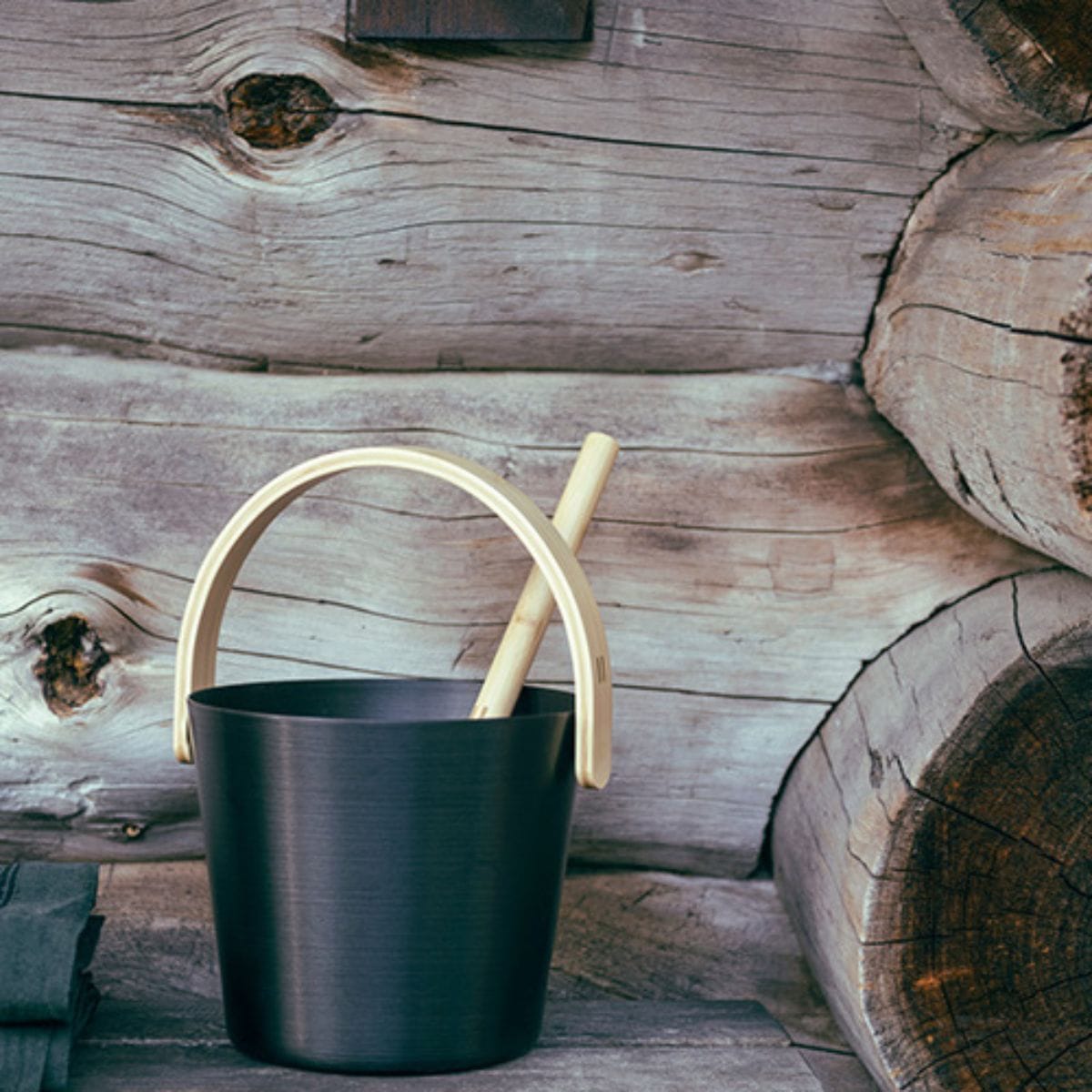 Black bucket with wooden handle and ladle against a wooden background