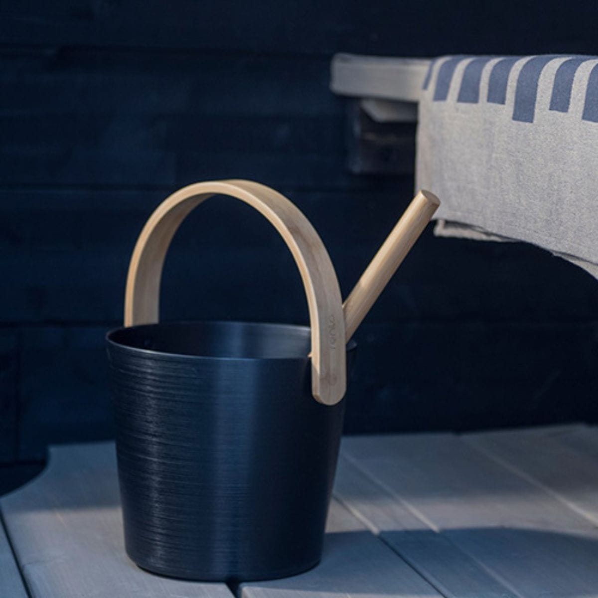 Black watering can with wooden handle on a wooden surface