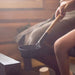 Person sitting in a sauna holding a wooden-handled aluminum ladle