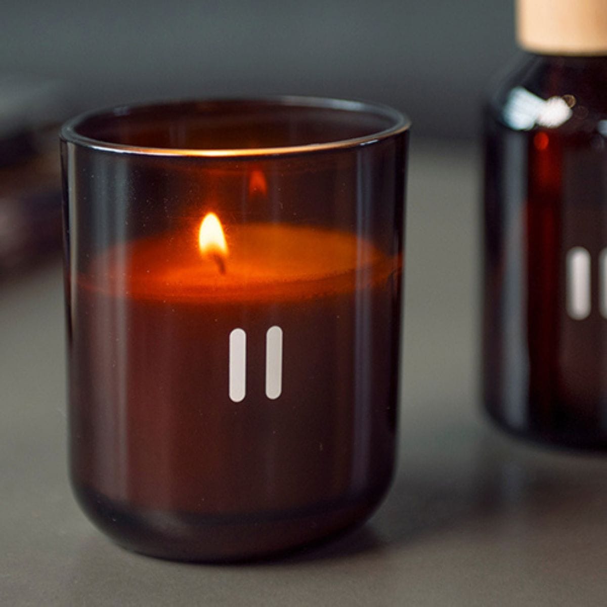 Amber glass candle with a lit wick on a neutral background