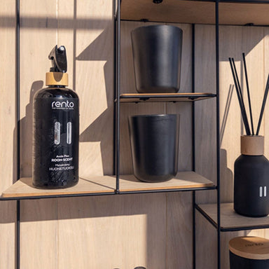 Black room scent bottle with gold cap on a wooden shelf with black containers and diffuser.