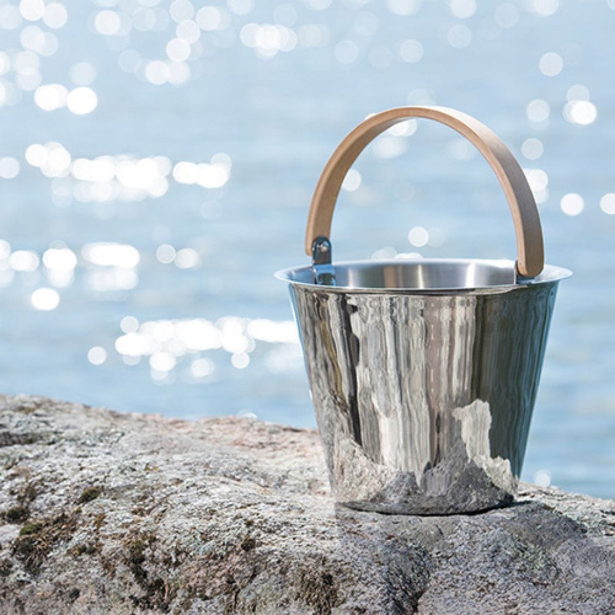 Metal bucket with wooden handle on a rock by a body of water