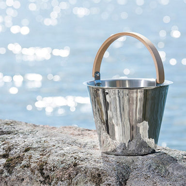 Metal bucket with wooden handle on a rock by a body of water