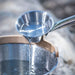 Metallic ladle pouring water into a pot with a blurred background