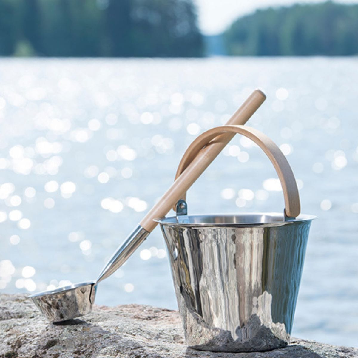 Metal bucket with wooden handle and ladle on a rock by a lake