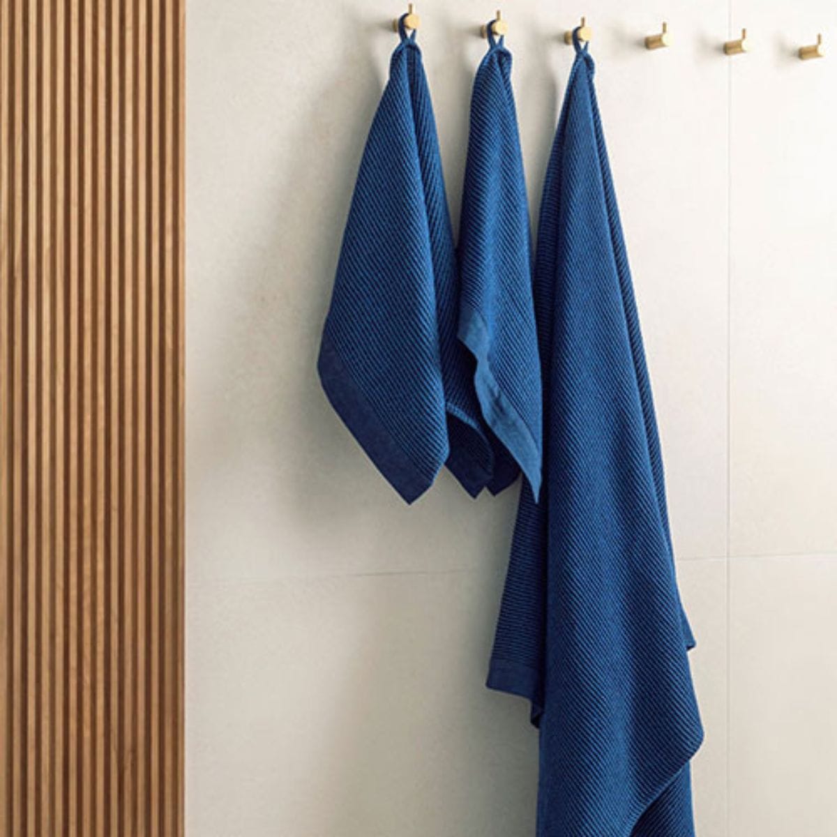 Three blue towels hanging on a rack against a neutral wall.