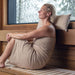 Woman wrapped in a towel sitting in a sauna with a snowy outdoor view.