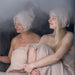 Two women in a steam room with hats wrapped around their heads and bodies.