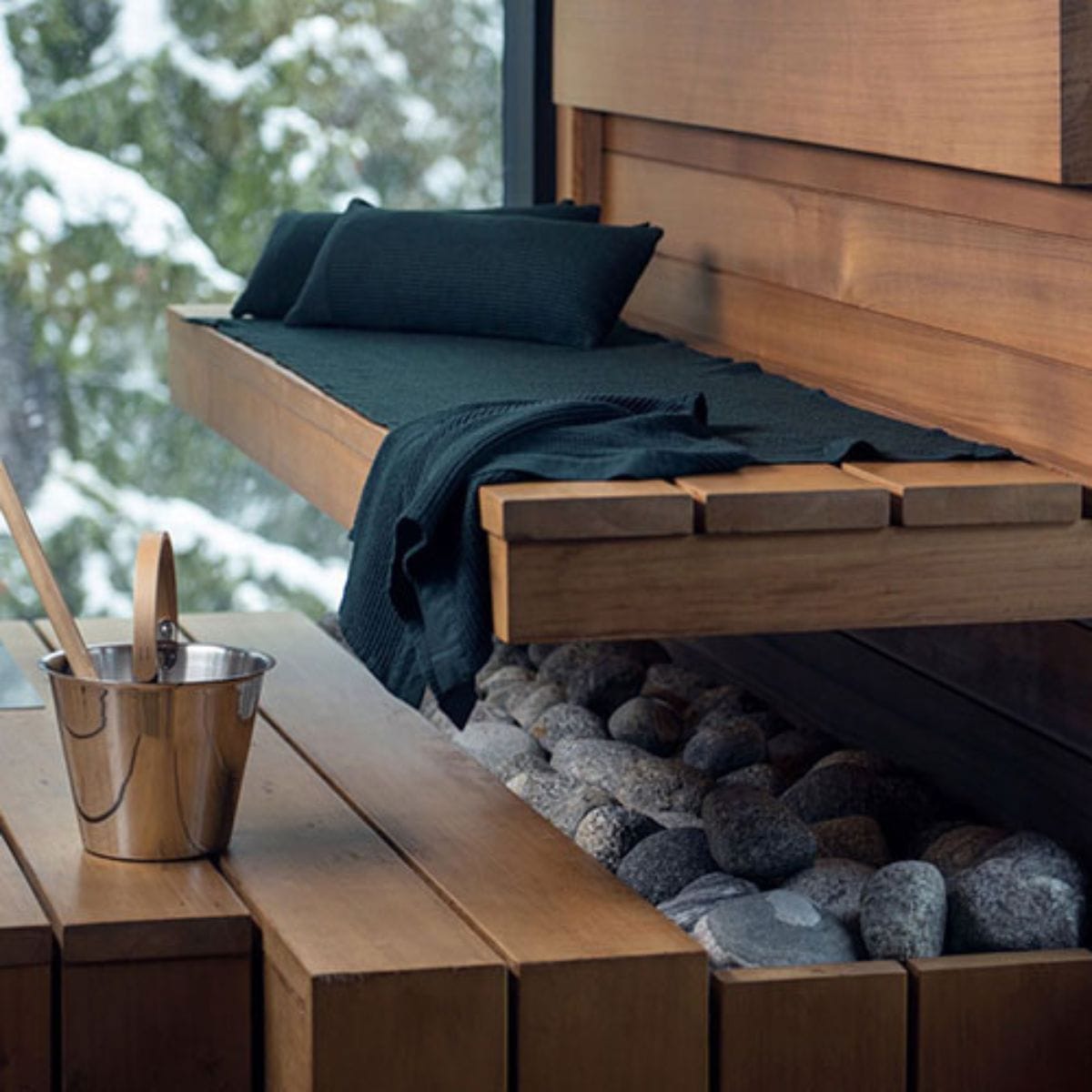 Wooden bench with cushions and a blanket, set against a snowy outdoor background.