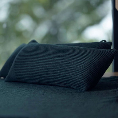 Dark green textured pillow on a blurred natural background