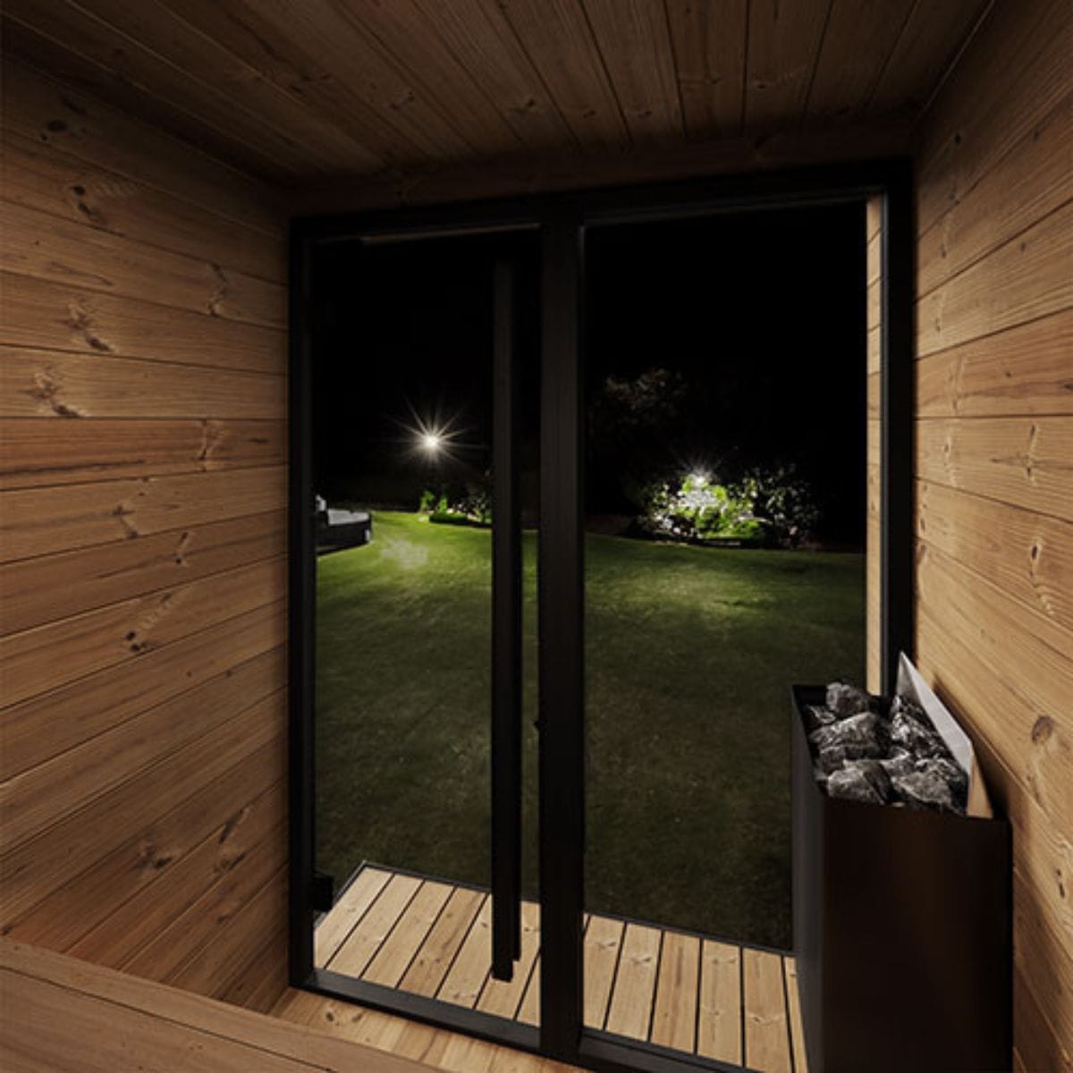 Wooden sauna with glass door open to a dark outdoor garden at night.
